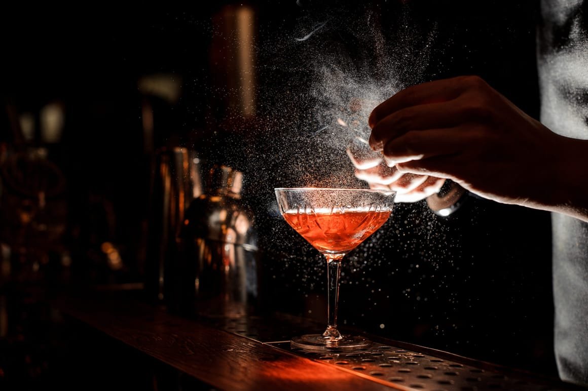 Barmans hands sprinkling the juice into the cocktail glass